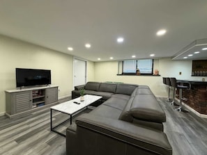 A modern living room with a sectional sofa, a flat-screen TV, a coffee table, and a bar area with stools.