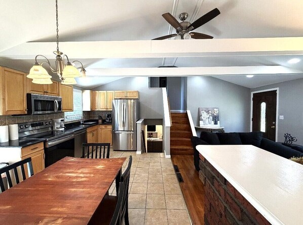 A modern kitchen with a dining area, a staircase, and a living area with a sofa.