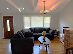 A living room with a sectional sofa, a coffee table, a fireplace, and a chandelier.