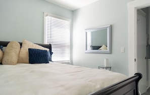 Un dormitorio con cama, almohadas, una mesita de noche, un espejo y una puerta.