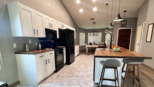 A modern kitchen with white cabinets, black appliances, and a wooden island with bar stools. - Modern Glendale Getaway /Mins from I-17 & 101 / 6 Flags, Hiking & Golf close by (Glendale)