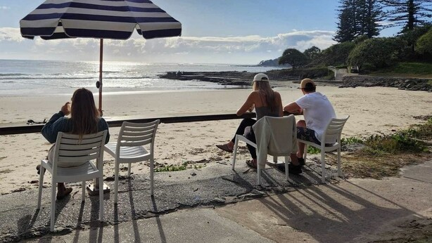 Un área de estar frente a la playa, con sombrillas a rayas y sillas, con vista al océano.