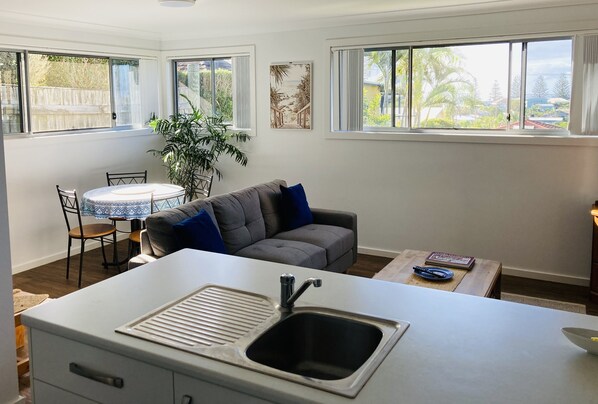 A compact kitchen with a sink, dining table, and gray sofa.