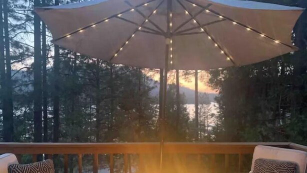 Una terraza con un pozo de fuego, mobiliario exterior y una sombrilla que proporciona sombra.