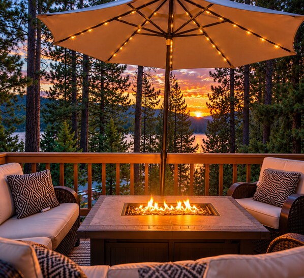 An outdoor deck with a fire feature, seating, and a view of a sunset over a body of water. - Shoreline cabin with lake views & boat slip (Bass Lake)