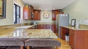Una cocina con encimeras de granito, armarios de madera, un refrigerador de acero inoxidable y un reloj en la pared.