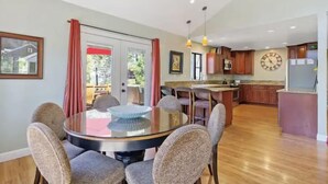 Una cocina moderna con armarios de madera, una isla central y una zona de comedor con una mesa y sillas de vidrio.