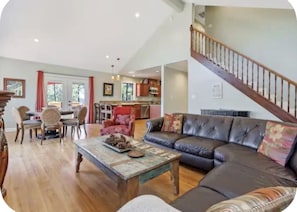 A spacious living room with a leather sofa, a coffee table, and a staircase leading to an upper level. - Shoreline cabin with lake views & boat slip (Bass Lake)