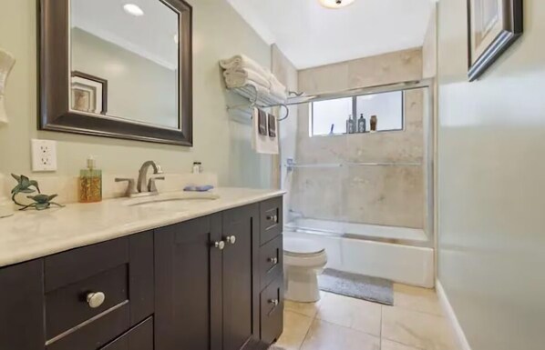 Un baño moderno con un espejo grande, gabinetes oscuros, un lavabo blanco y una zona de ducha.