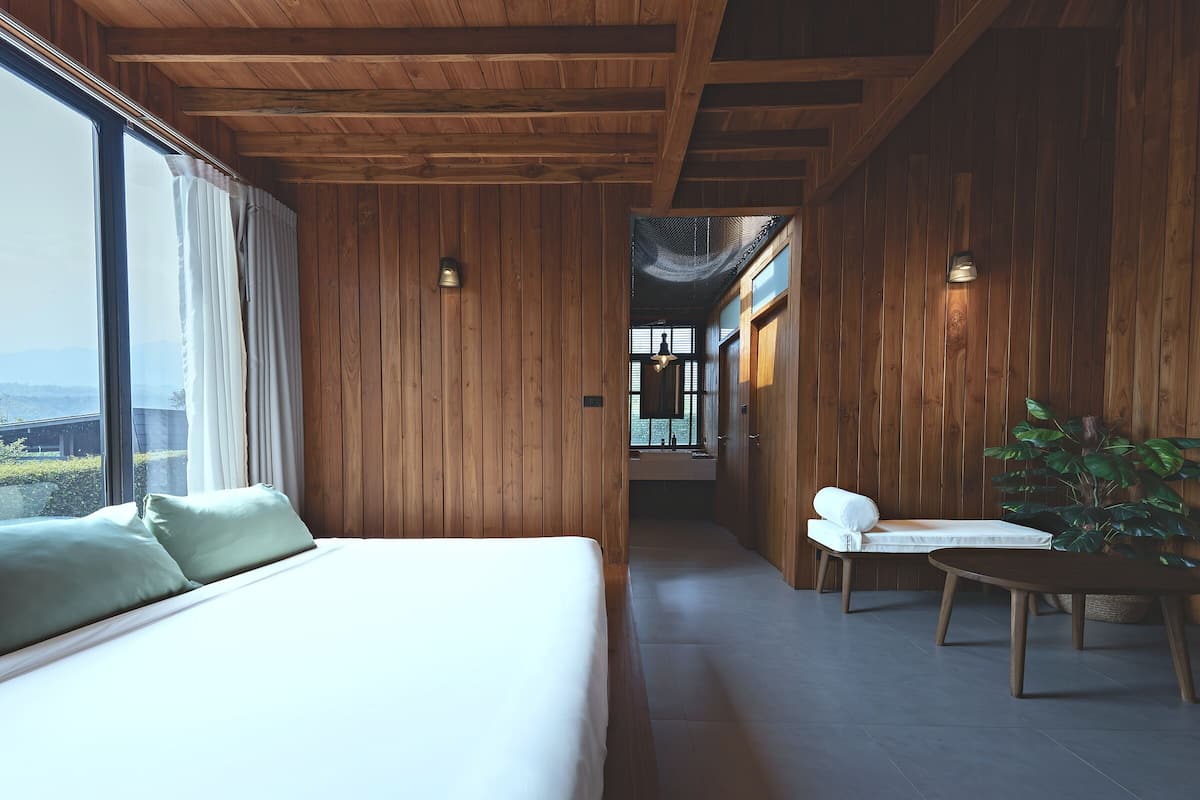 A bedroom with a large bed, a chair, a table, and a view of the outdoors.