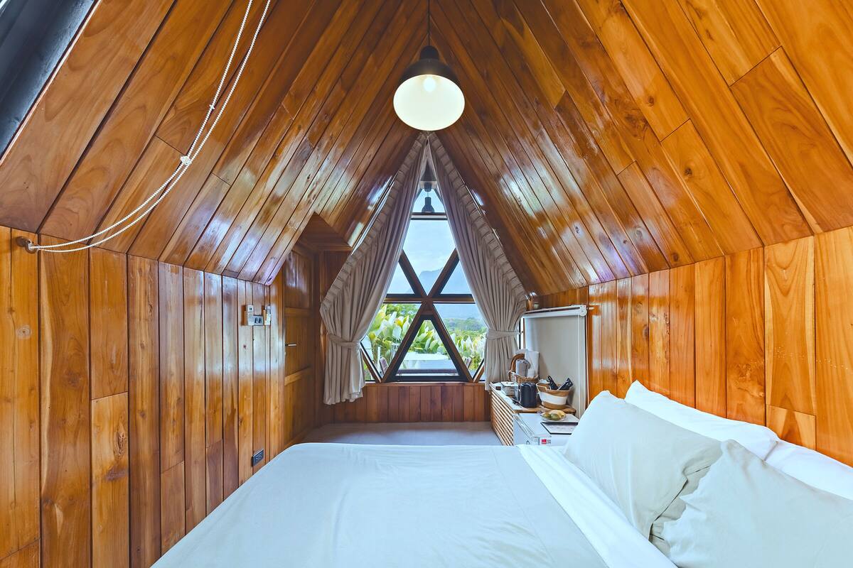 A wooden room with a bed, a window, and a ceiling light.