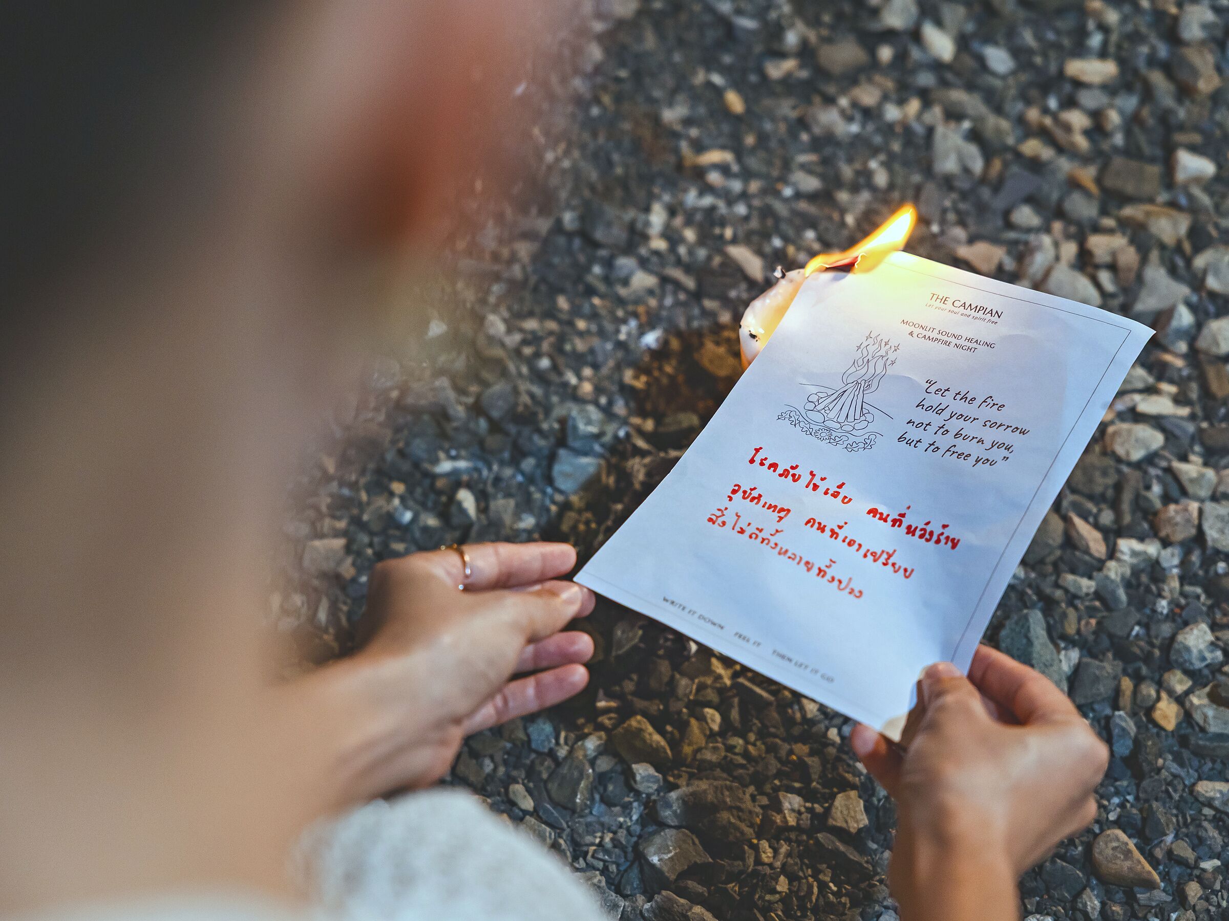 A person holding a lit candle with a paper that has text and a drawing.