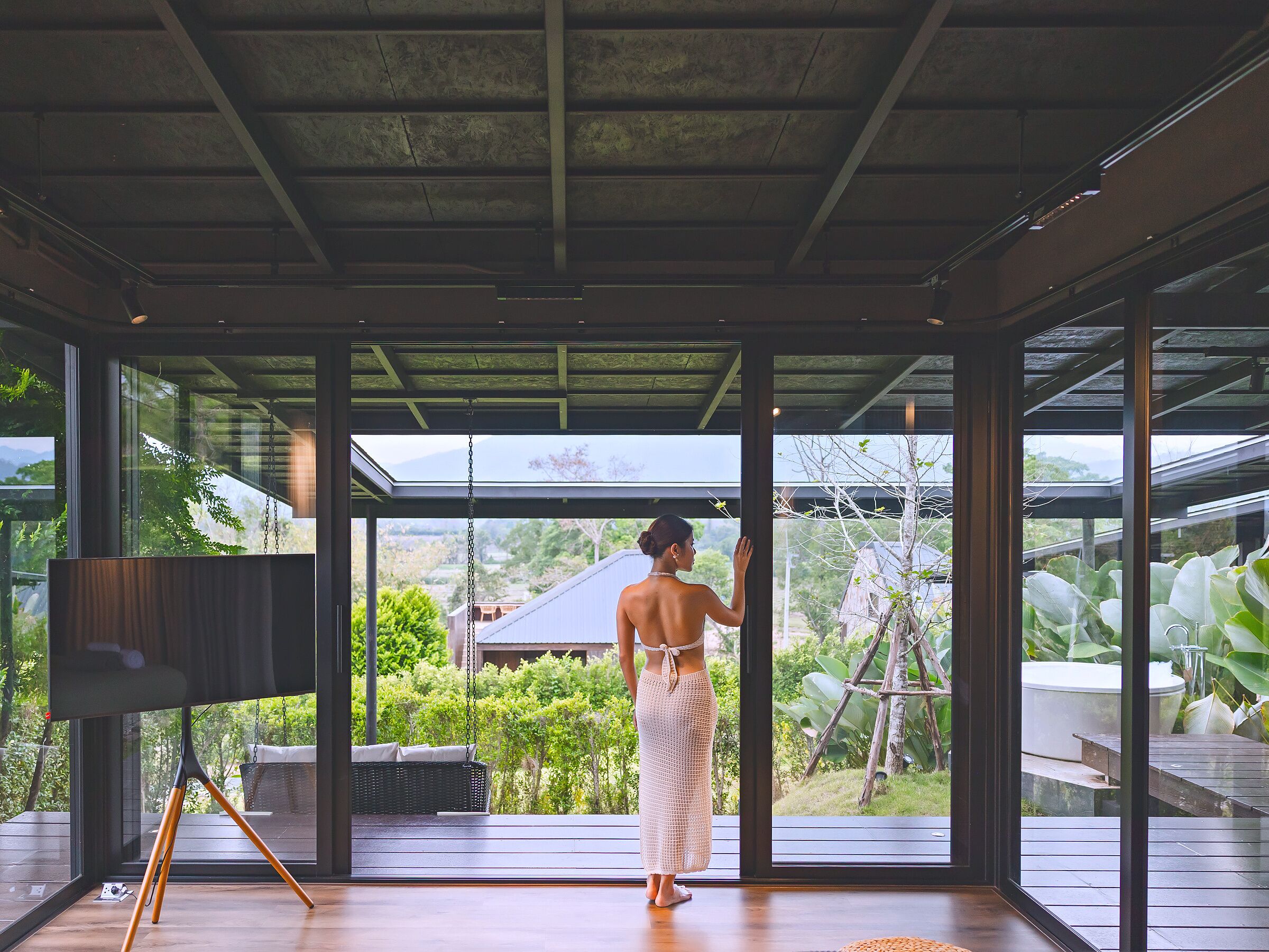 A spacious room with a large window, a television on a stand, and a view of a lush garden.