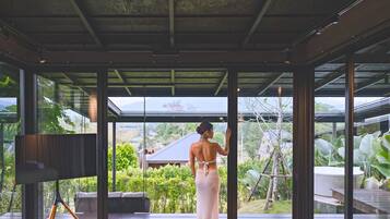 A spacious room with a large window, a television on a stand, and a view of a lush garden.