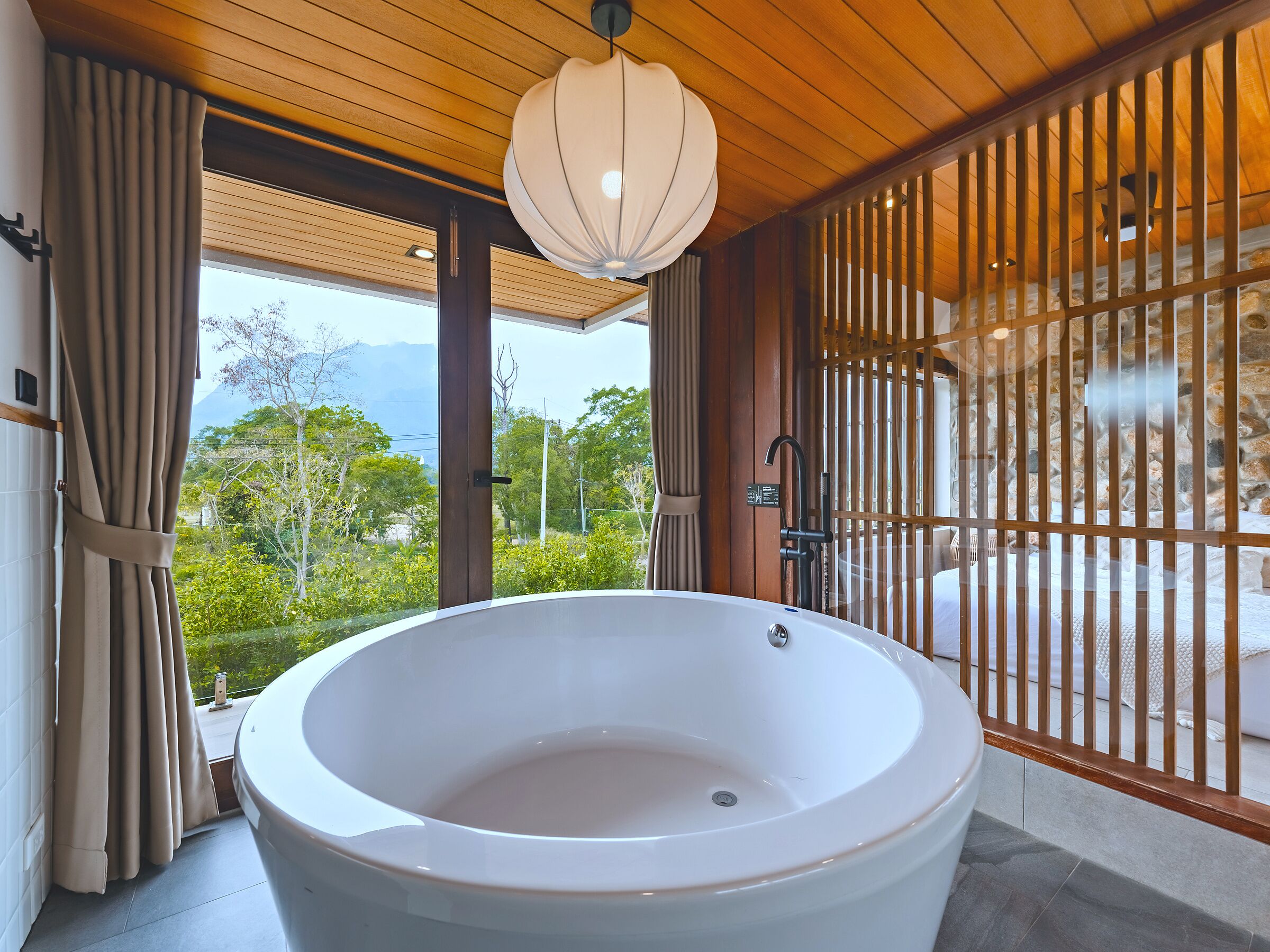 A large bathtub in a room with wooden ceiling and a view of greenery and mountains.