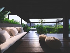 A modern outdoor seating area with a sofa and ottoman, surrounded by lush greenery and a view of distant mountains.