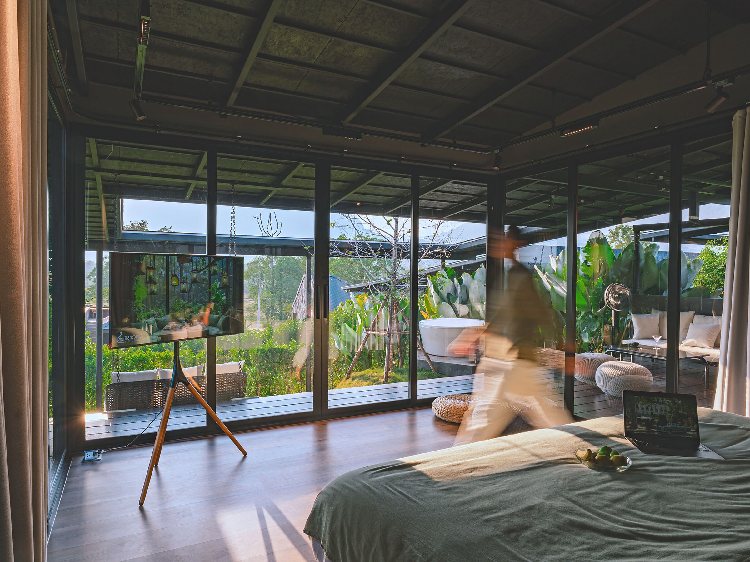 A modern room with large windows, a bed, a laptop, and a dining area.