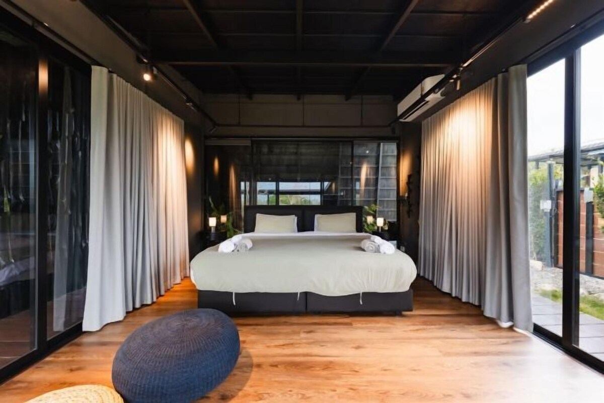 Un dormitorio moderno con una cama grande, cortinas y vistas a través de las paredes de cristal.