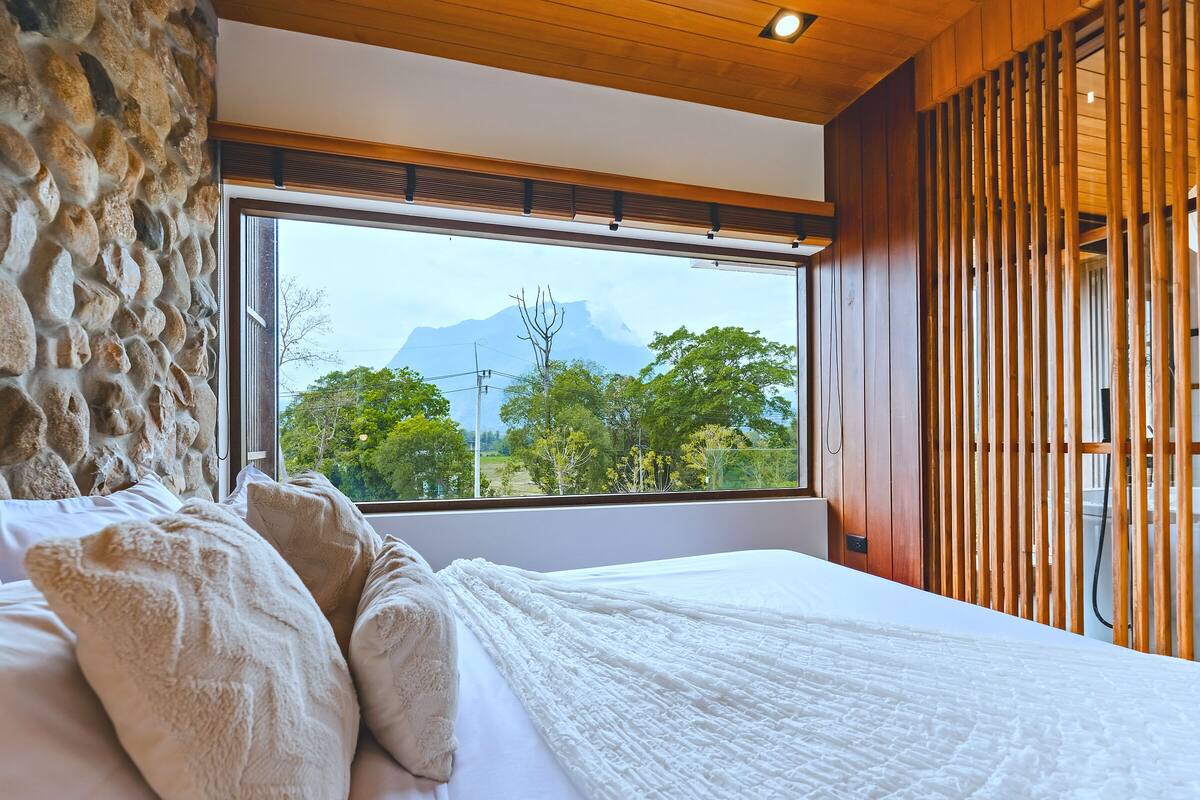 A bedroom with a large window, a stone wall, and wooden paneling.