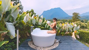 Una mujer en una bañera al aire libre, con vistas a la montaña.