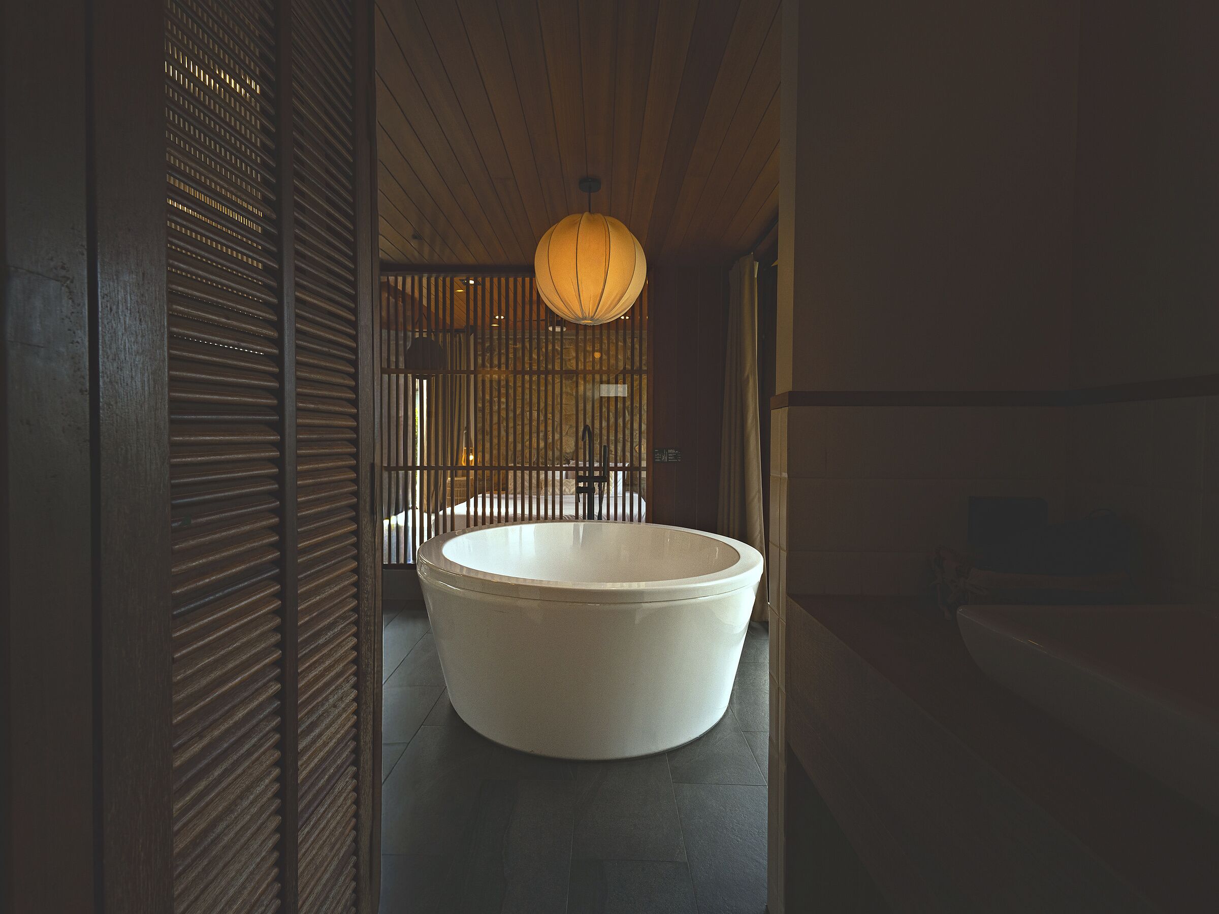 A modern bathroom with a large bathtub, wooden ceiling, and a hanging light fixture.