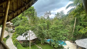A lush garden with a pool, stone pathways, and traditional wooden structures. - The Osing Bamboo Resort - Banyuwangi (Banyuwangi)