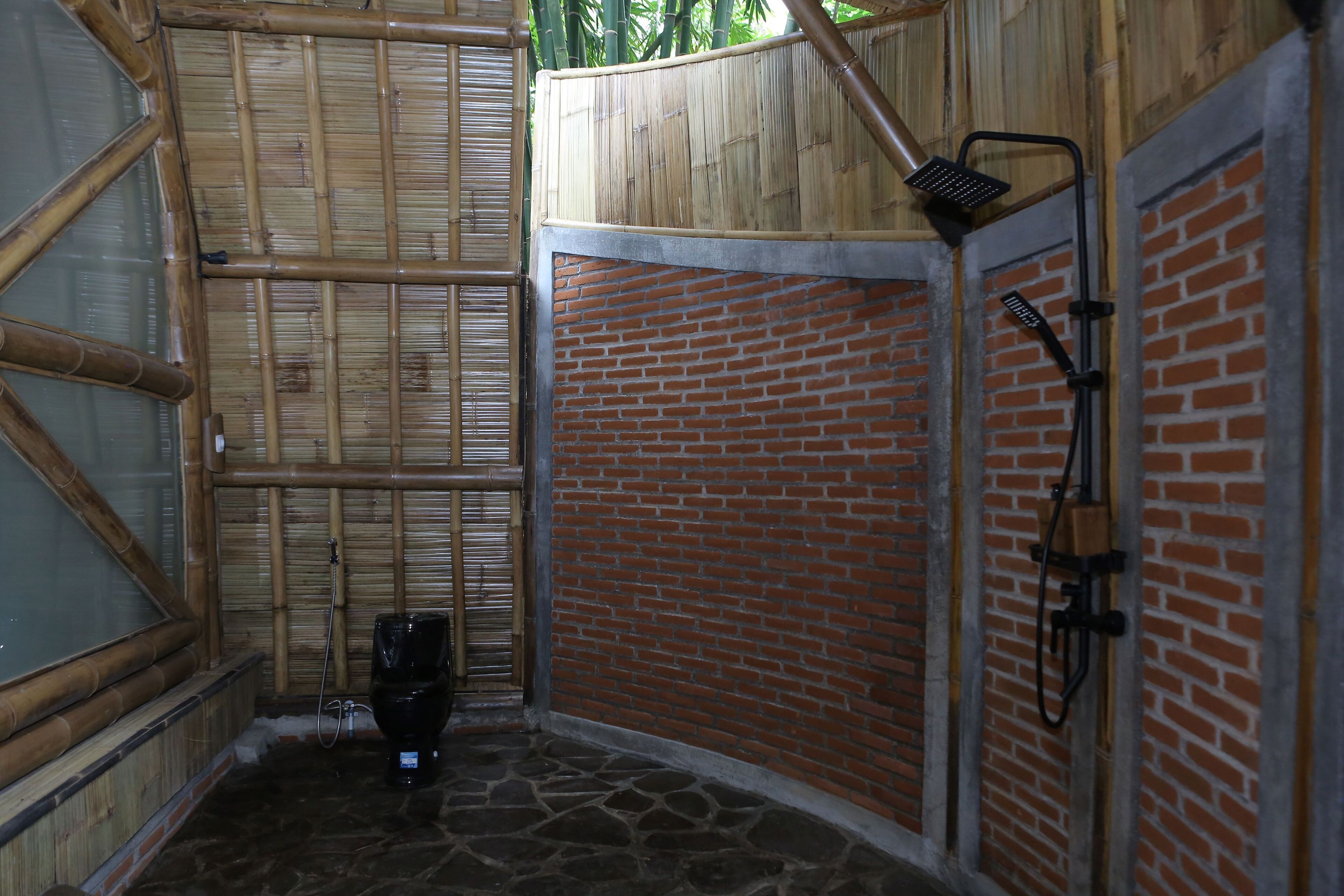 A bamboo-framed shower area with a brick wall and a stone floor.