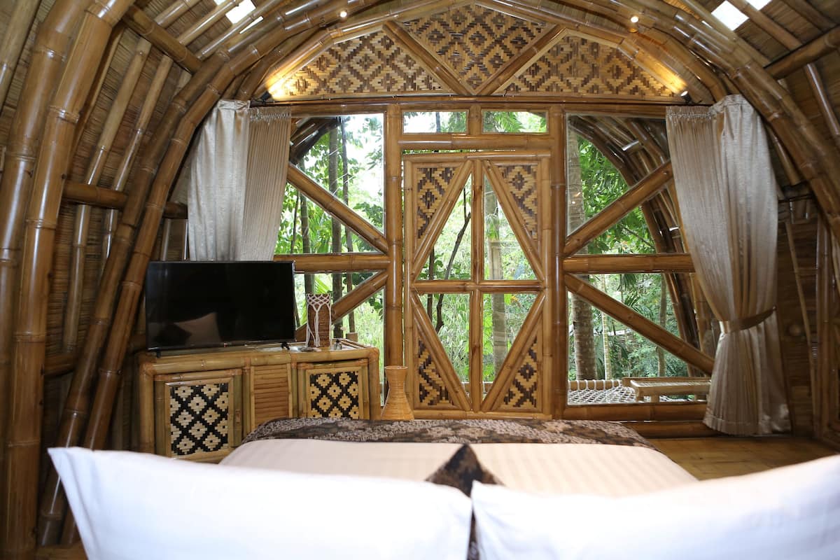 Ein Zimmer mit einem großen Bett, einem Fernseher und einem Fenster mit Blick auf Bäume.