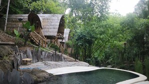 A rustic wooden structure with a stone pathway leading to a pool surrounded by dense greenery. - The Osing Bamboo Resort - Banyuwangi (Banyuwangi)