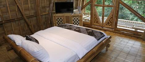 A room with a bed, a television on a wooden nightstand, and large windows with a view of greenery.