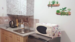 A compact kitchen with a marble-patterned cabinet, a microwave, and a dishwasher. There are wooden cabinets, a sink, and a countertop. - Amourette's Studio at Mesaavirre Garden (Bacolod)