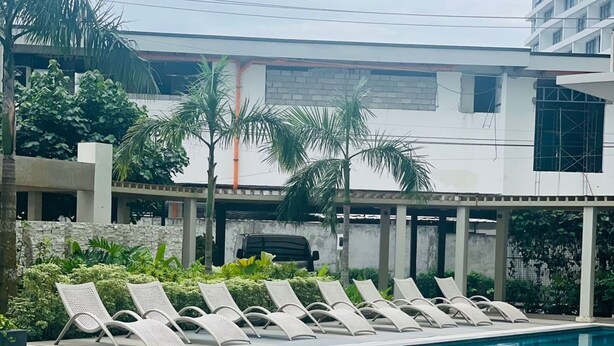 A swimming pool with lounge chairs, surrounded by greenery and a modern building. - Amourette's Studio at Mesaavirre Garden (Bacolod)