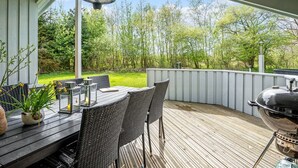 An outdoor patio with a wooden deck, a table with chairs, a grill, and a hanging light fixture. - "Bjart" - 1.5km from the sea by Interhome (Væggerløse)
