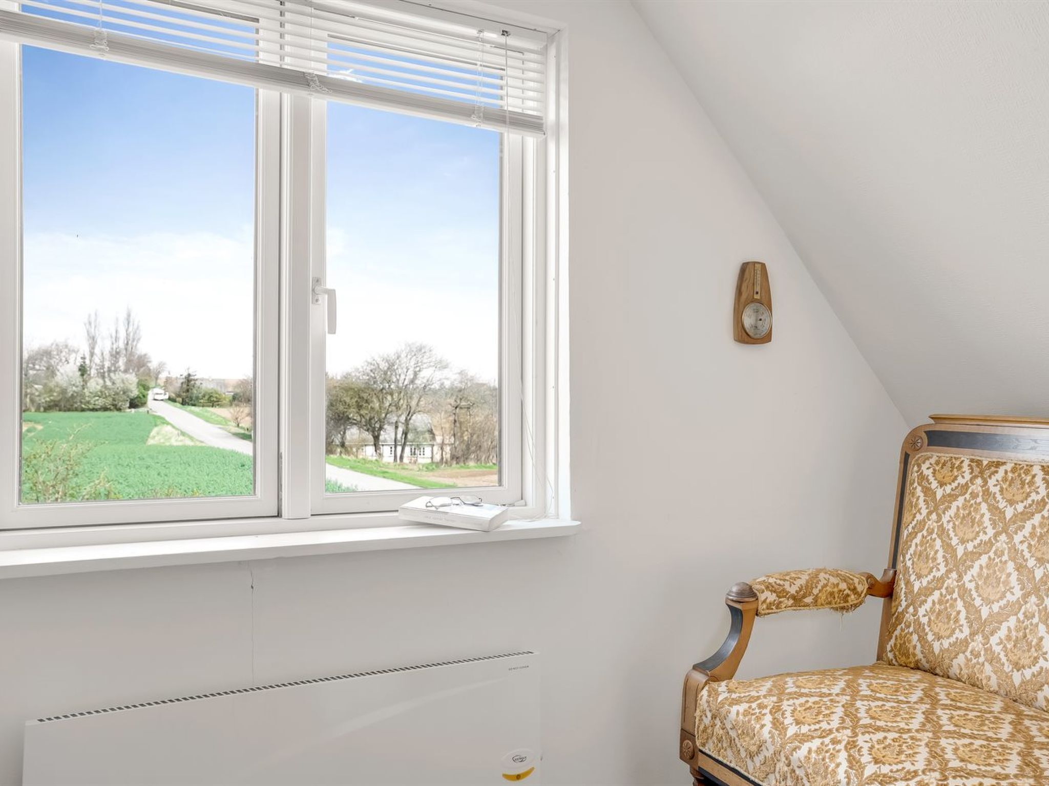 A room with a large window, a radiator, and a patterned armchair.