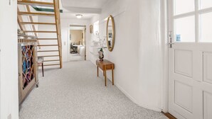 A hallway with a wooden ladder, a mirror, a small table with a vase, and a door with a window.
