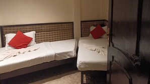 Two single beds with white linens and red pillows, a wooden door with a number plate, and a small framed picture on the wall. - Hotel Serene (Shillong)