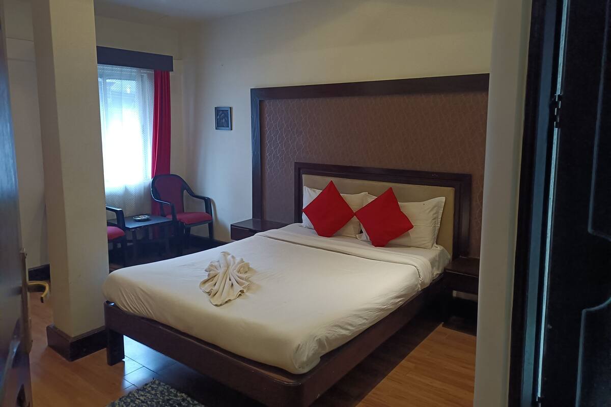 A hotel room with a bed, a chair, a small table, and a window with curtains.
