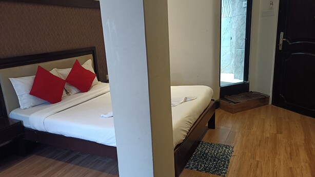 A hotel room with a bed, a wooden floor, a window, and a door. - Hotel Serene (Shillong)