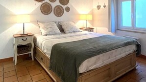 A bedroom with a wooden bed, two bedside tables with lamps, a wall with woven decorations, and a window with blinds. - Cosy old Nice Appartement (Nice)