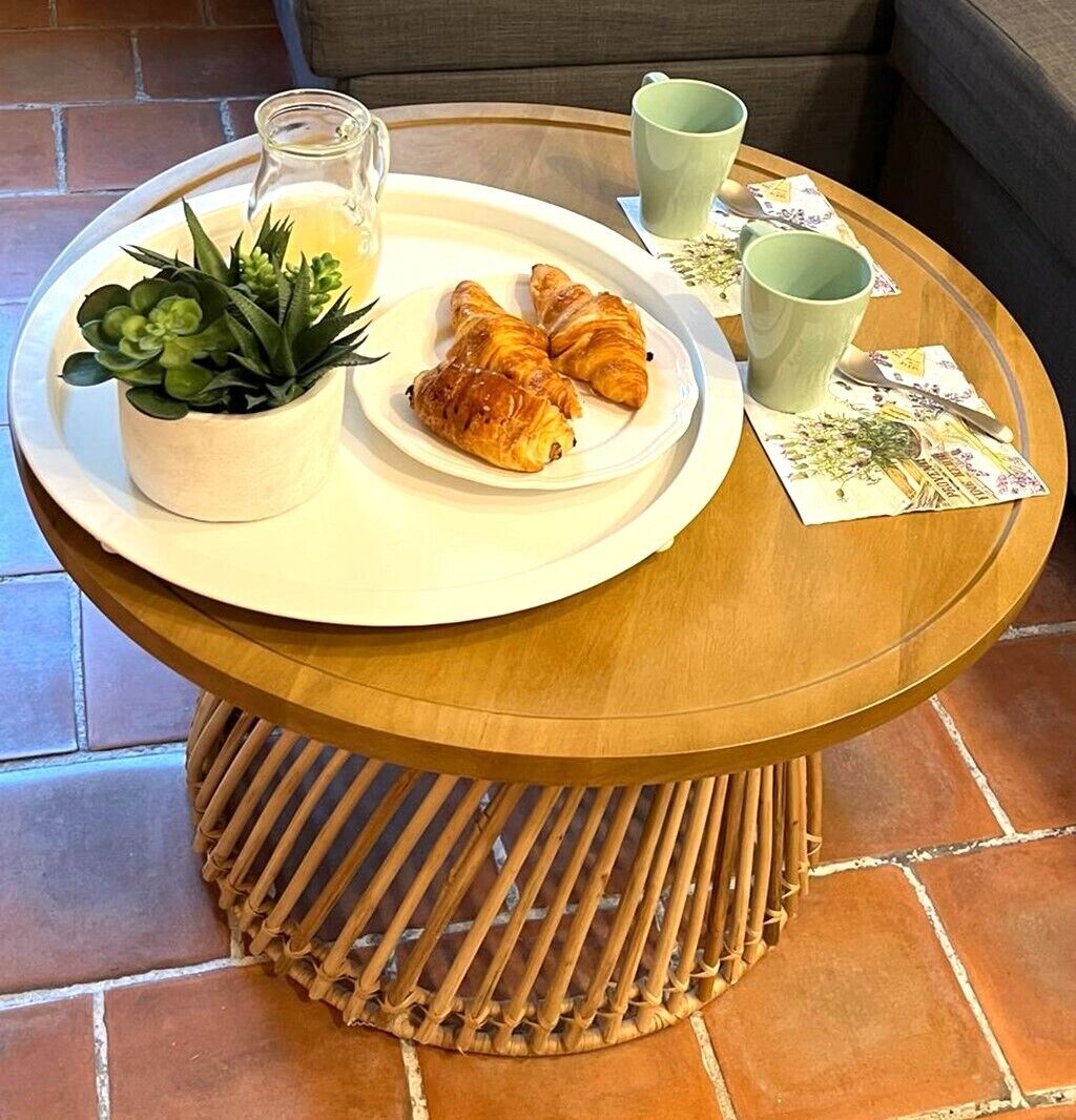 Een ontbijtje met croissants, een kleine plant, een glas sap en een groene mok op een ronde houten tafel met een geweven onderzetter.