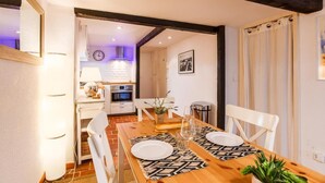 A dining area with a wooden table set for two, white chairs, and a kitchen in the background. - Cosy old Nice Appartement (Nice)