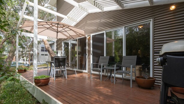 Een overdekt terras buiten met houten vloer, metalen stoelen en een tafel.