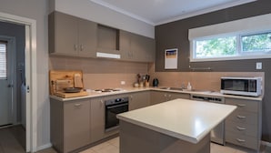 Een moderne keuken met grijze kastjes, een centraal eiland, een magnetron en een raam met uitzicht op groen.