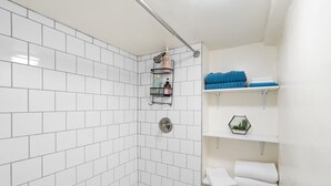Un baño moderno con paredes de azulejos blancos, zona de ducha y estantes empotrados con toallas y artículos de aseo.