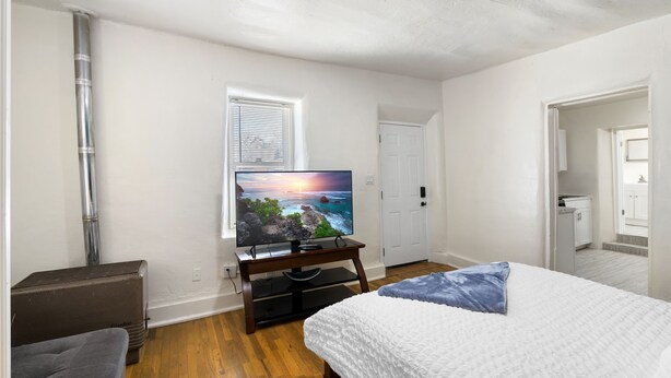 Un dormitorio con cama, televisión sobre un mueble, ventana y puerta.