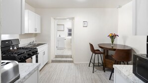 Una cocina compacta con armarios blancos, una estufa y un comedor con dos sillas y una mesa.