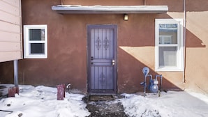 Una casa de color marrón, con una puerta gris y un diseño decorativo, y un ventanal pequeño con marco blanco.