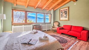 A bedroom with a large bed, a red sofa, a window with a view, and a radiator. - Faby House On Hilly Area And Lake View (Gargnano)