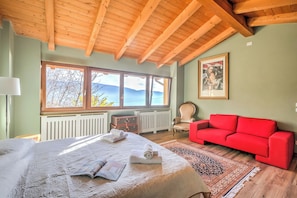 A bedroom with a large bed, a red sofa, a window with a view, and a radiator.