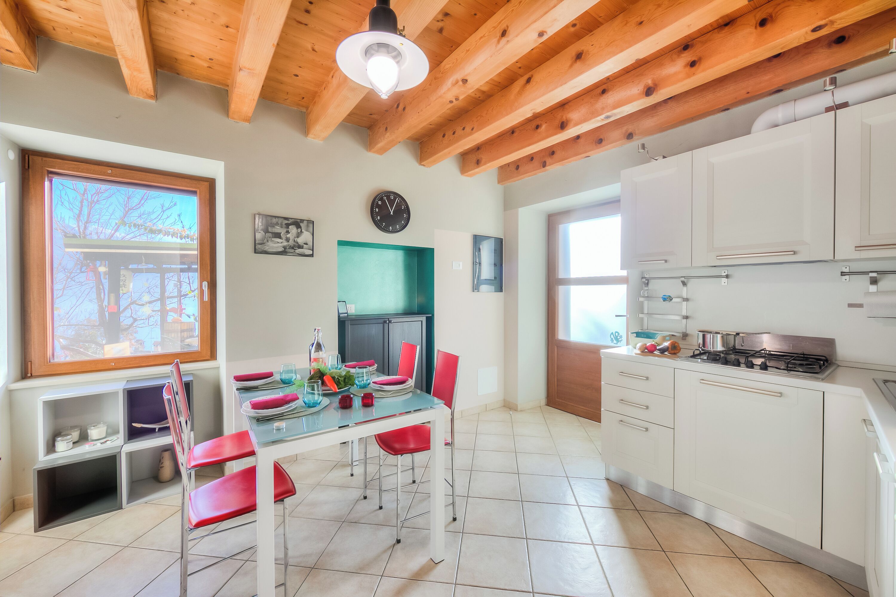 A modern kitchen with white cabinets, a gas stove, and a dining area with red chairs and a glass table.